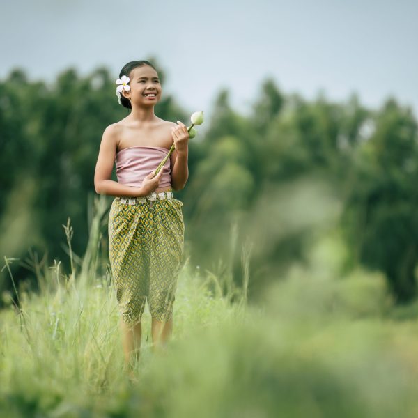 Portrait of lovely girls in Thai traditional dress and put white flower on her ear,  Standing and hold two lotus in hand on rice field, She smile with happiness and looking camera, copy space